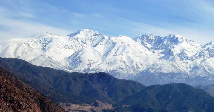 Die gewaltige, schneebedeckte Südwand des Aconcagua über dunklen Vorbergen unter blauem Himmel